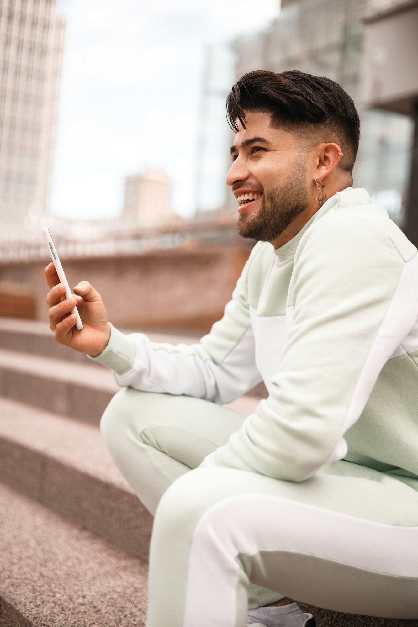 happy hispanic young man in sportswear using cellphone in urban scenario, big closeup view