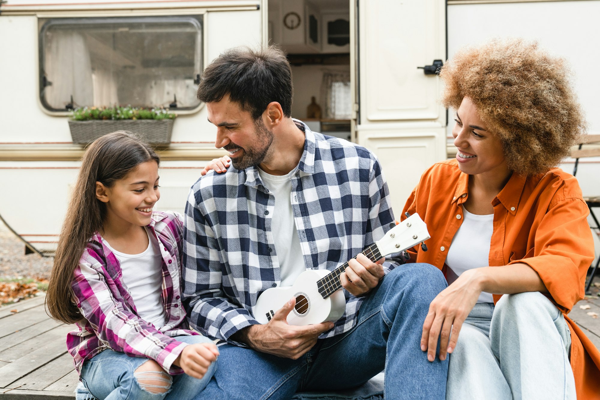 Happy interracial family of three with daughter kid playing ukulele together while traveling by van